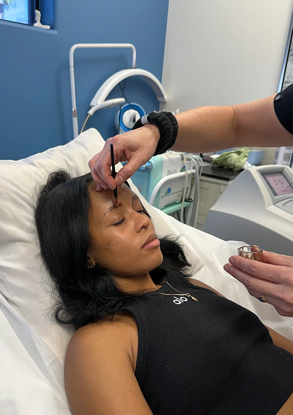 Aesthetician applying brow tint to client's eyebrow during treatment in medical spa