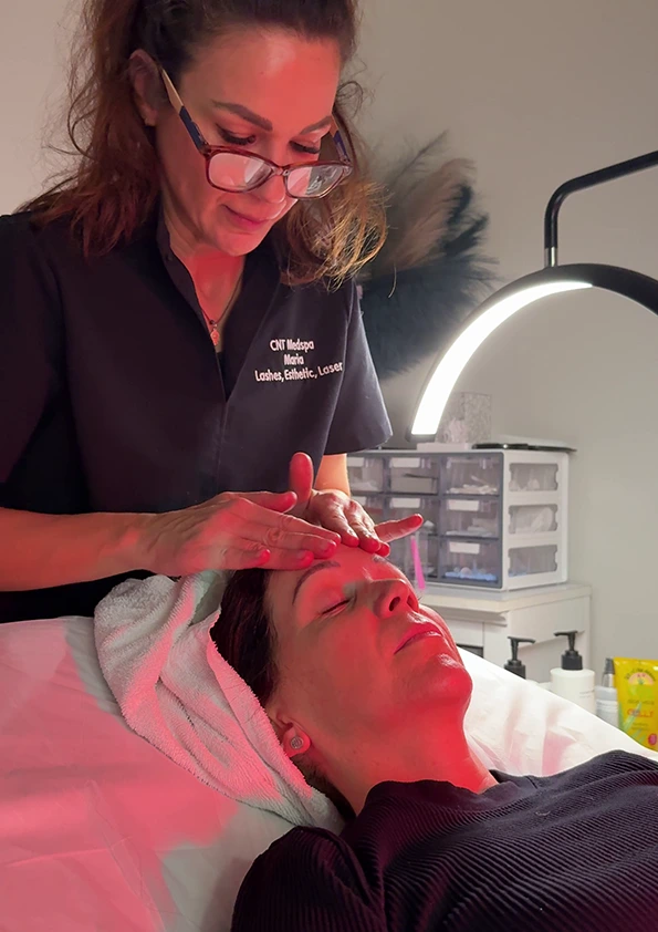 Provider performing red light facial treatment on relaxed patient under therapeutic lamp