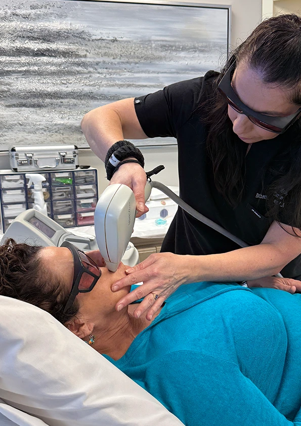 Practitioner using handheld laser device for hair removal on client's face
