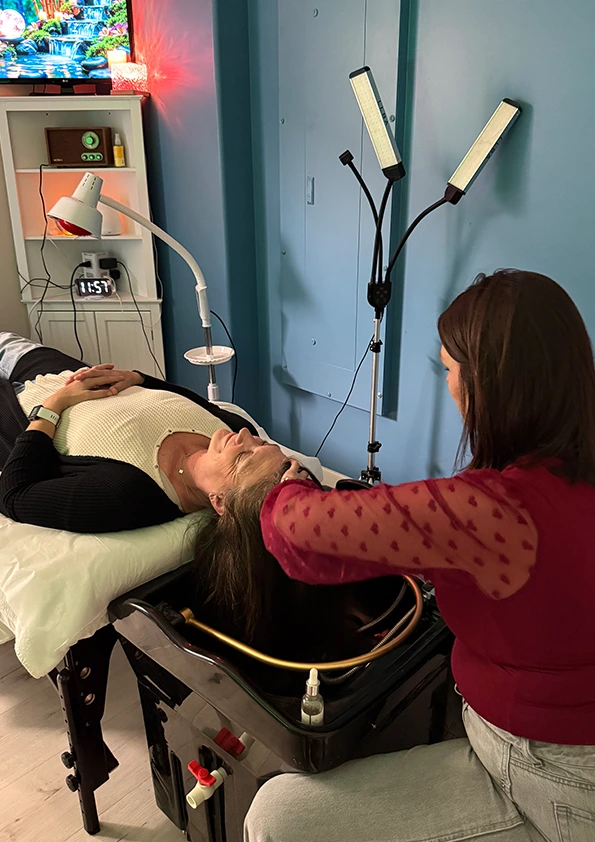 Aesthetician performing head spa treatment on reclined patient with dual LED light therapy device