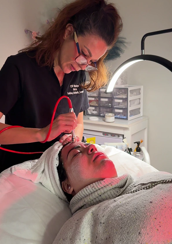 Provider administering HydraFacial treatment with red light device on patient's face