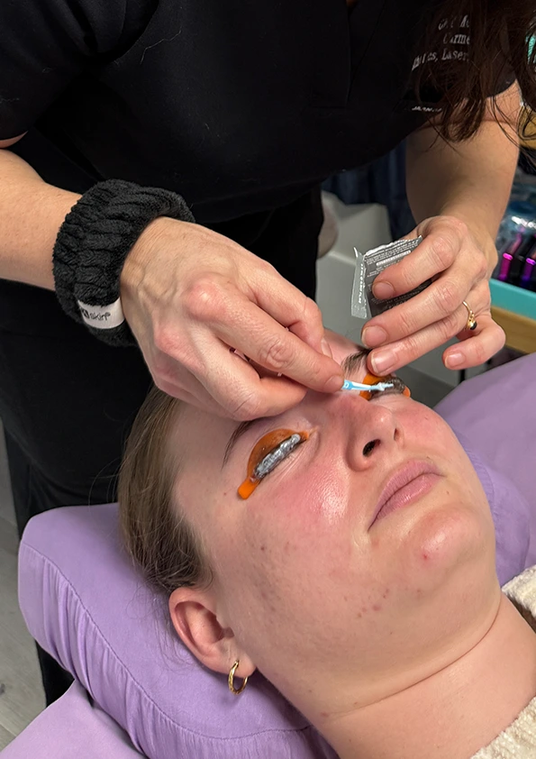 Aesthetician applying lash lift solution to client's lashes during treatment