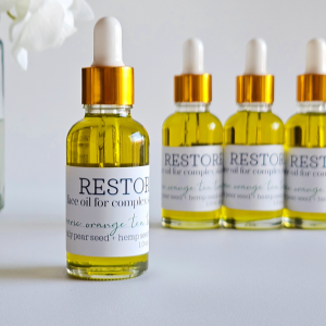 Restore face oil dropper bottle in foreground with gold cap and white pipette, three matching bottles behind it