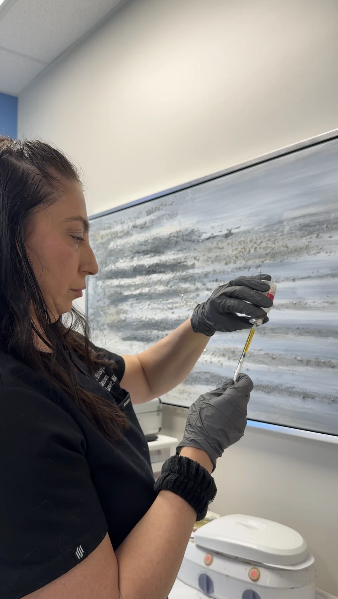 Clinician in black gloves preparing microneedling treatment with device next to window