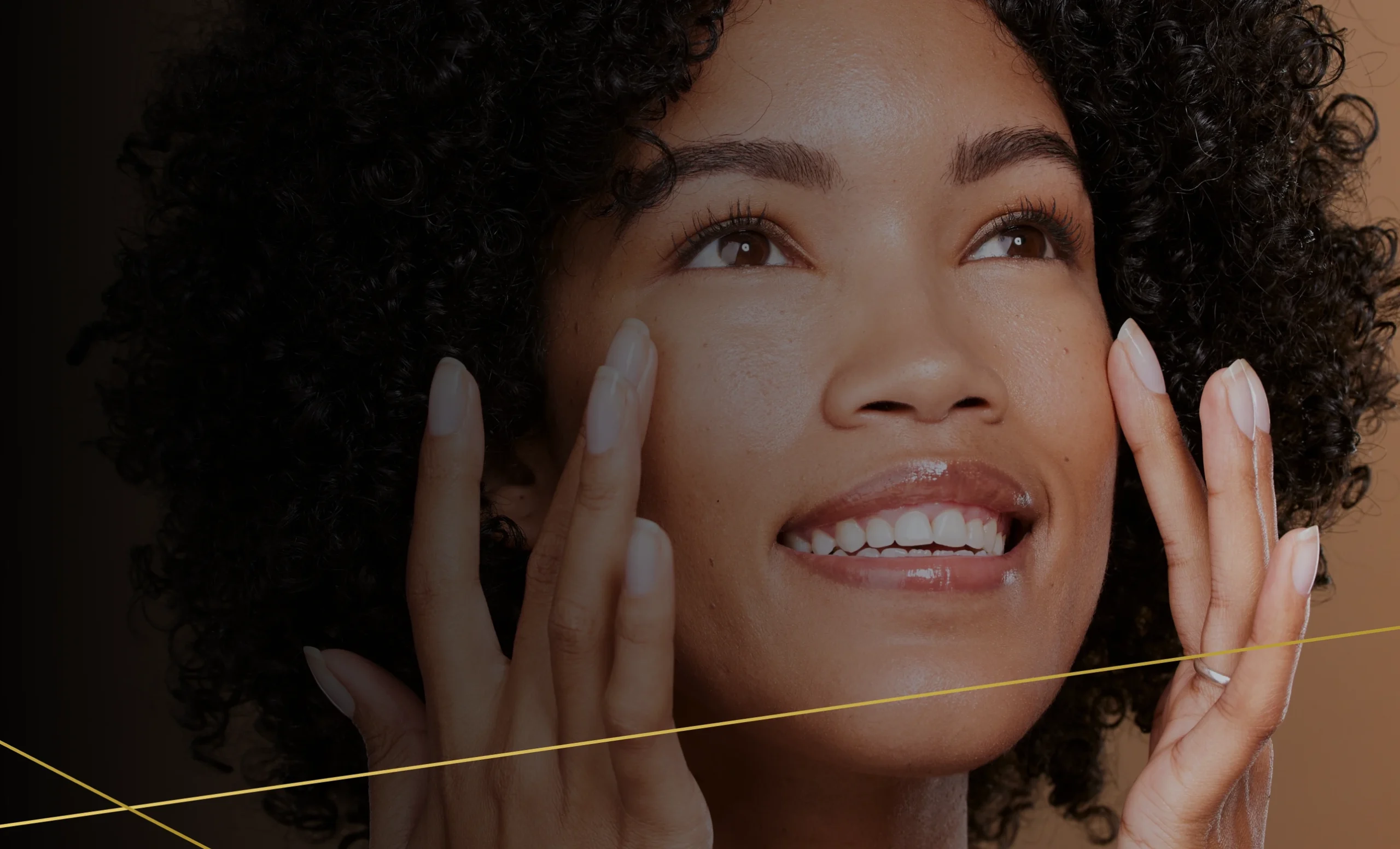 Smiling woman with curly hair touching her glowing, smooth skin