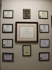Wall display of framed dental degrees and certifications from Temple University and professional organizations