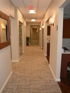 Well-lit hallway at Advanced Dentistry of Collegeville with treatment rooms on either side and exit sign overhead
