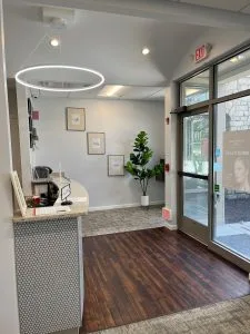 Modern reception area with circular pendant light, welcome desk, motivational wall art, potted plant, and glass entrance doors