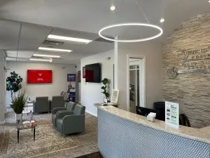 Modern dental reception area with front desk, seating area, and Advanced Dentistry of Collegeville logo on brick wall