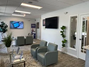 Advanced Dentistry of Collegeville waiting room with gray recliners, plants, wall-mounted TVs, and glass doors leading outside