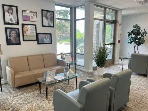Waiting room at Advanced Dentistry of Collegeville with tan and gray seating, framed provider photos on the wall, and large windows overlooking the street