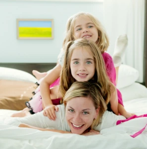 Mother and two daughters smiling together on a bed in a bright bedroom