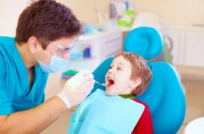 Dentist in blue scrubs treating a young child in a dental chair during a routine examination