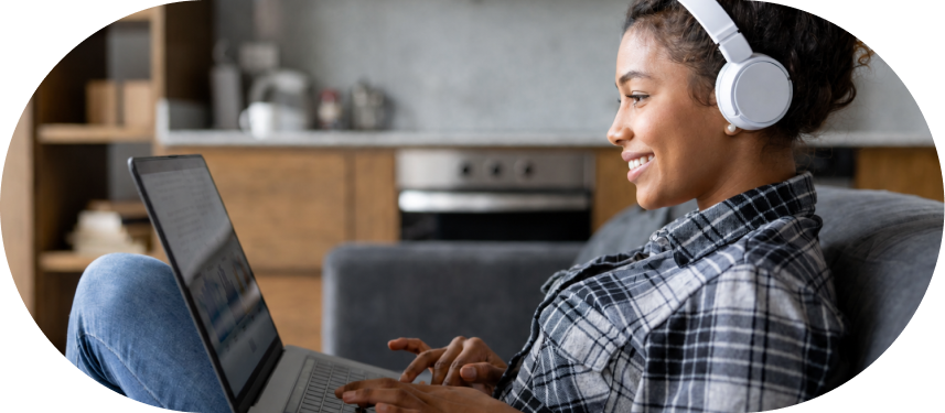 Woman wearing headphones typing on laptop while sitting on couch at home