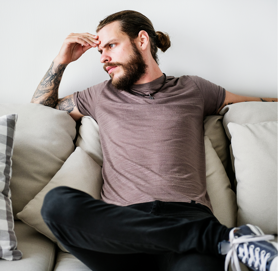 Man sitting on couch with hand to forehead, appearing stressed or contemplative