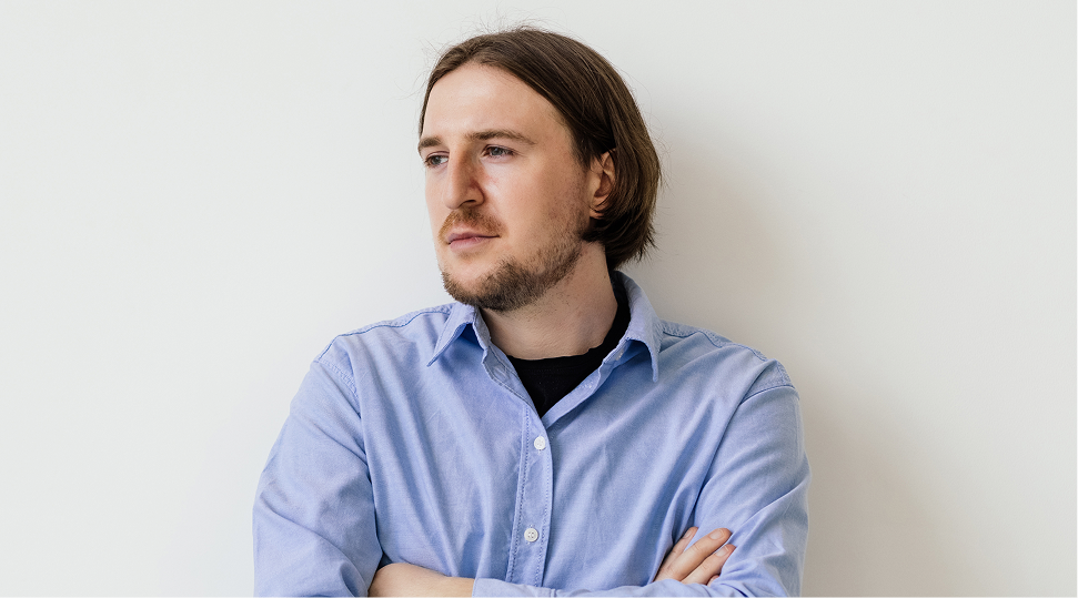 Man in light blue shirt with arms crossed, looking to the side against white background