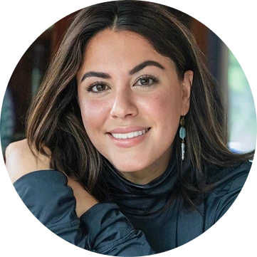 Smiling woman with long dark hair wearing a dark blue jacket and dangling earrings