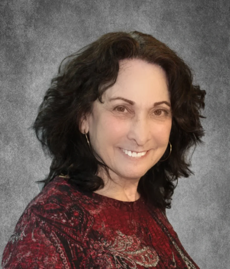 Woman with dark wavy hair wearing burgundy top, smiling at camera