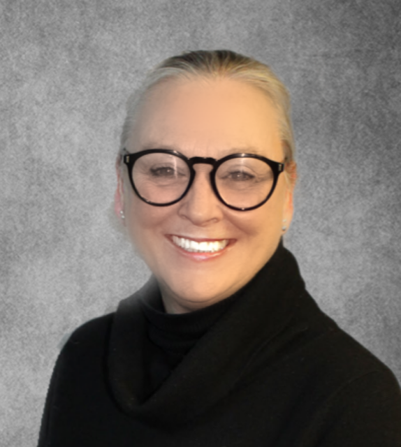 Woman with blonde hair wearing black-framed glasses and black top, smiling