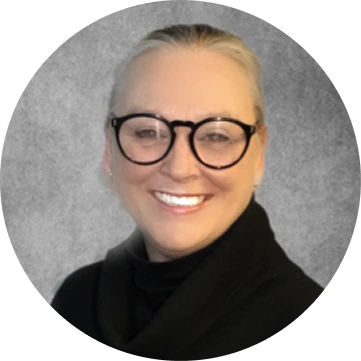 Woman with short blonde hair wearing black turtleneck and glasses smiling at camera
