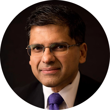 Professional headshot of a man wearing glasses and a purple tie against a dark background