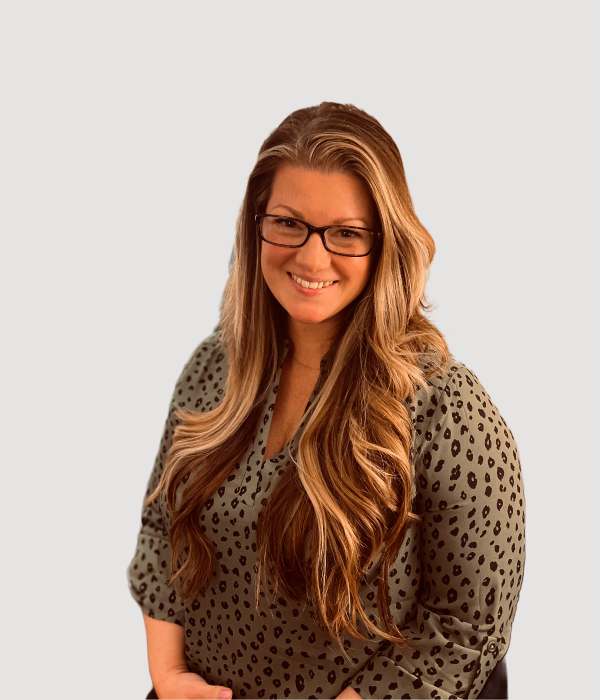 Marlyana, woman with long reddish-brown hair wearing glasses and a spotted blouse, smiling at camera