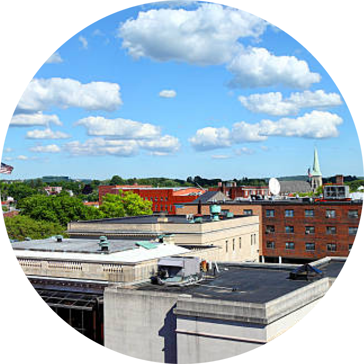Aerial view of brick buildings and tree-lined streets under blue sky with white clouds