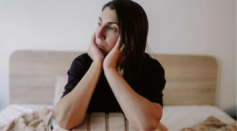Woman sitting on bed with hands to face, appearing thoughtful or contemplative