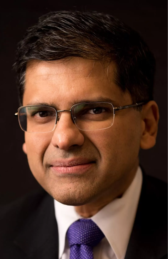 Professional headshot of man wearing glasses, white shirt, and purple tie