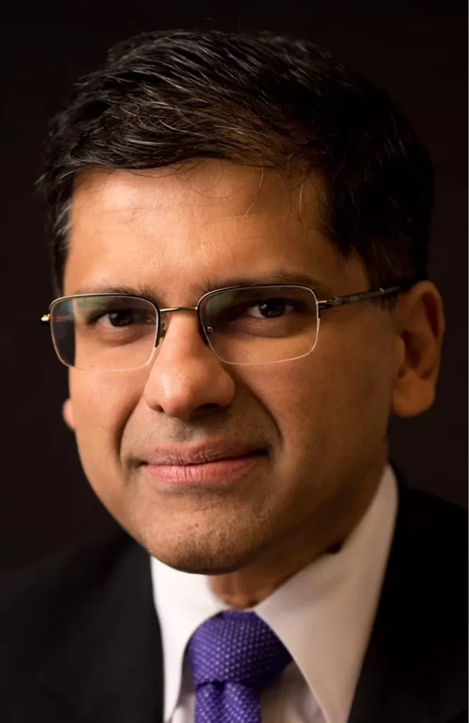 Professional headshot of man wearing glasses, white shirt, and purple tie