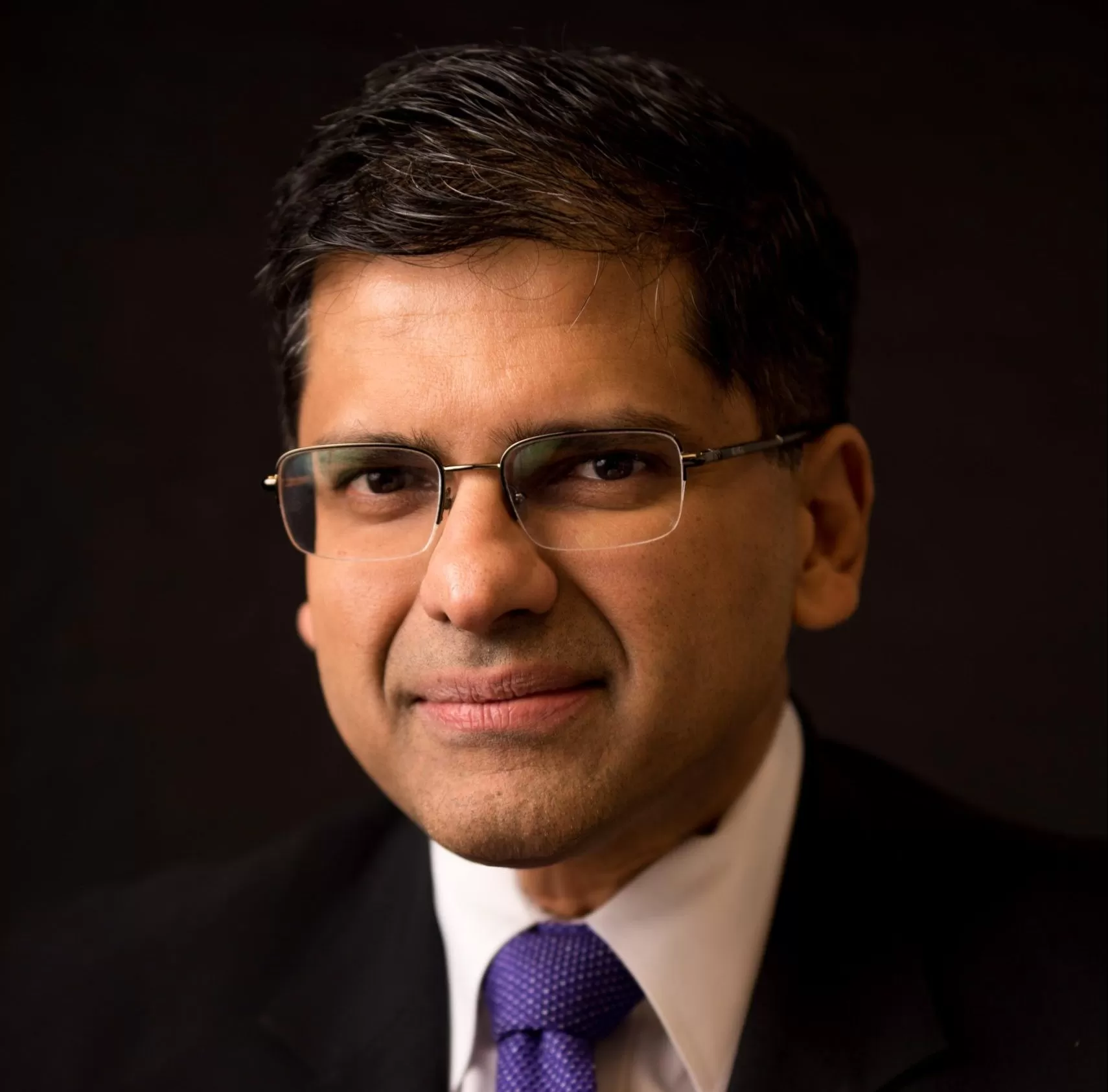 Man wearing glasses and dark suit with purple tie