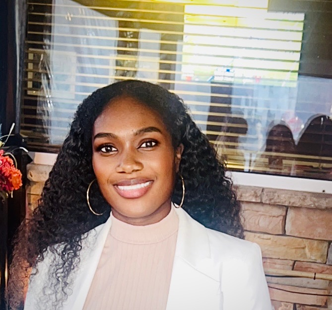 Tricia Ricketts, woman with long curly black hair and hoop earrings in white blazer, office background