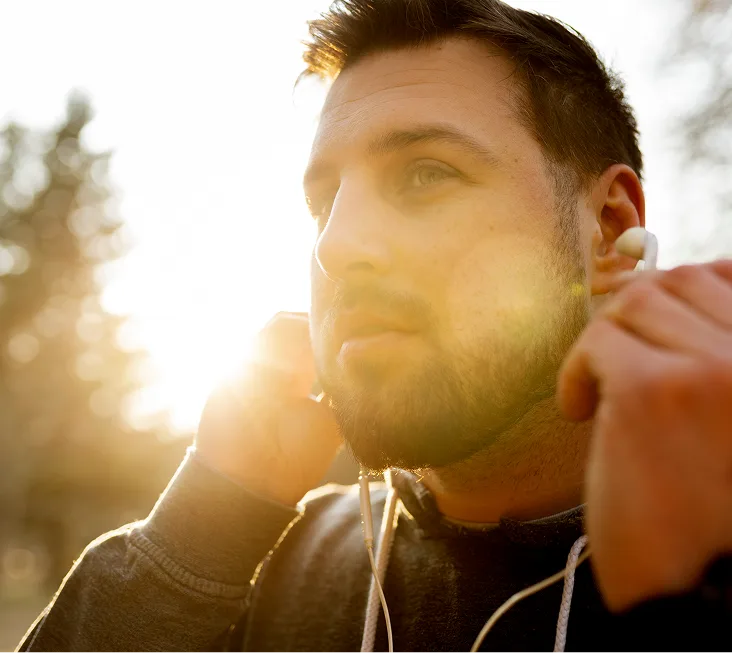Man with earbuds standing in bright sunlight
