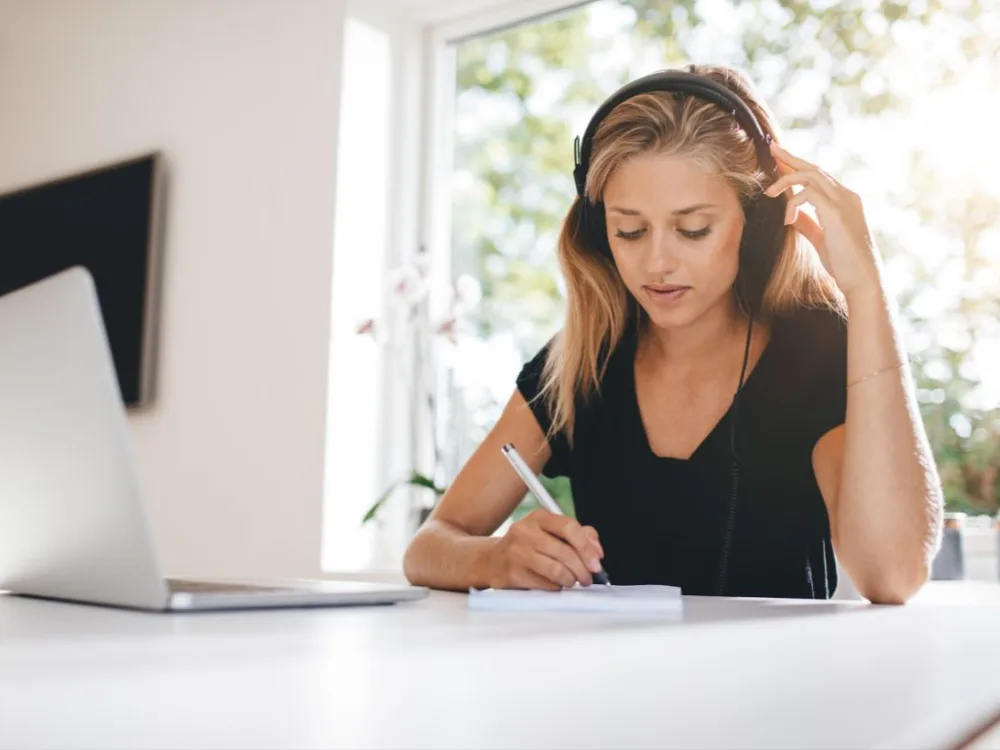 Woman with headphones taking notes at her laptop