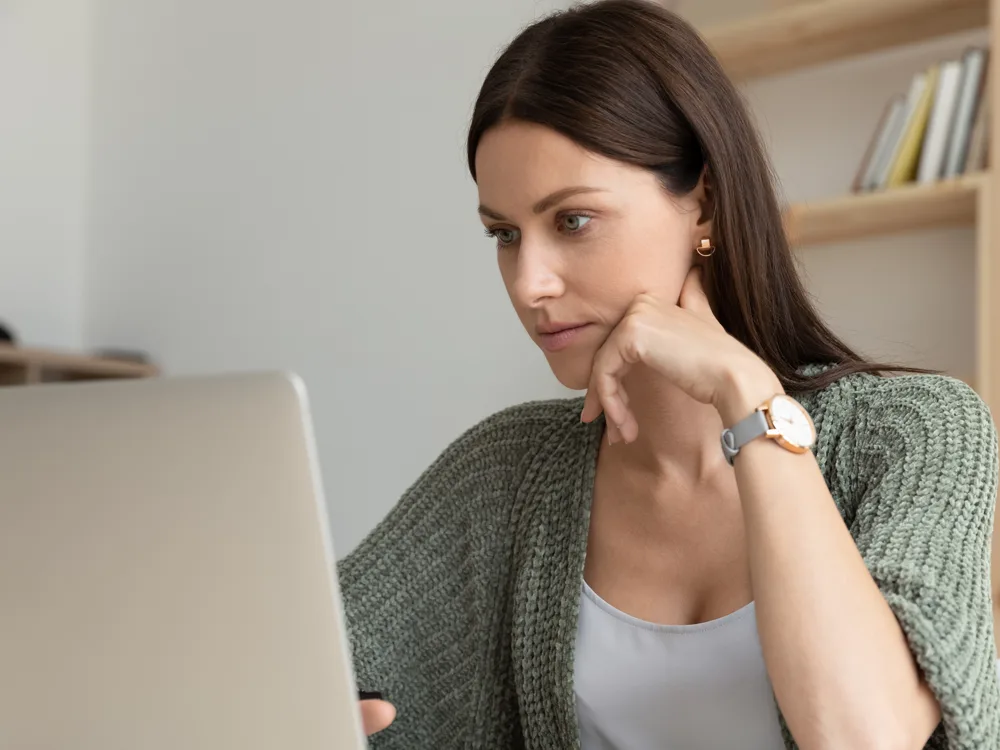Woman in a knit cardigan looking thoughtfully at her laptop