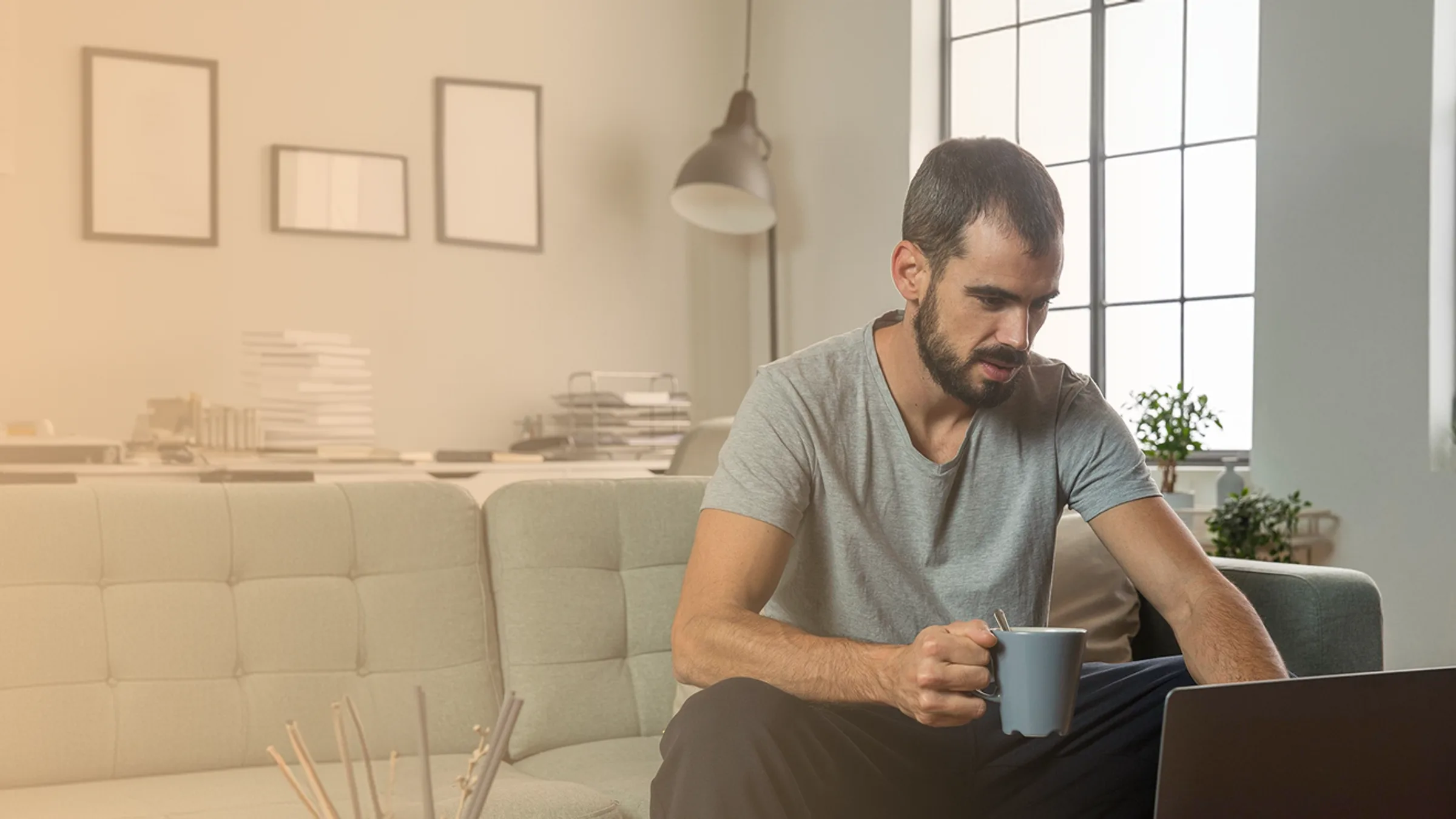 Man with a mug using his laptop on the sofa at home