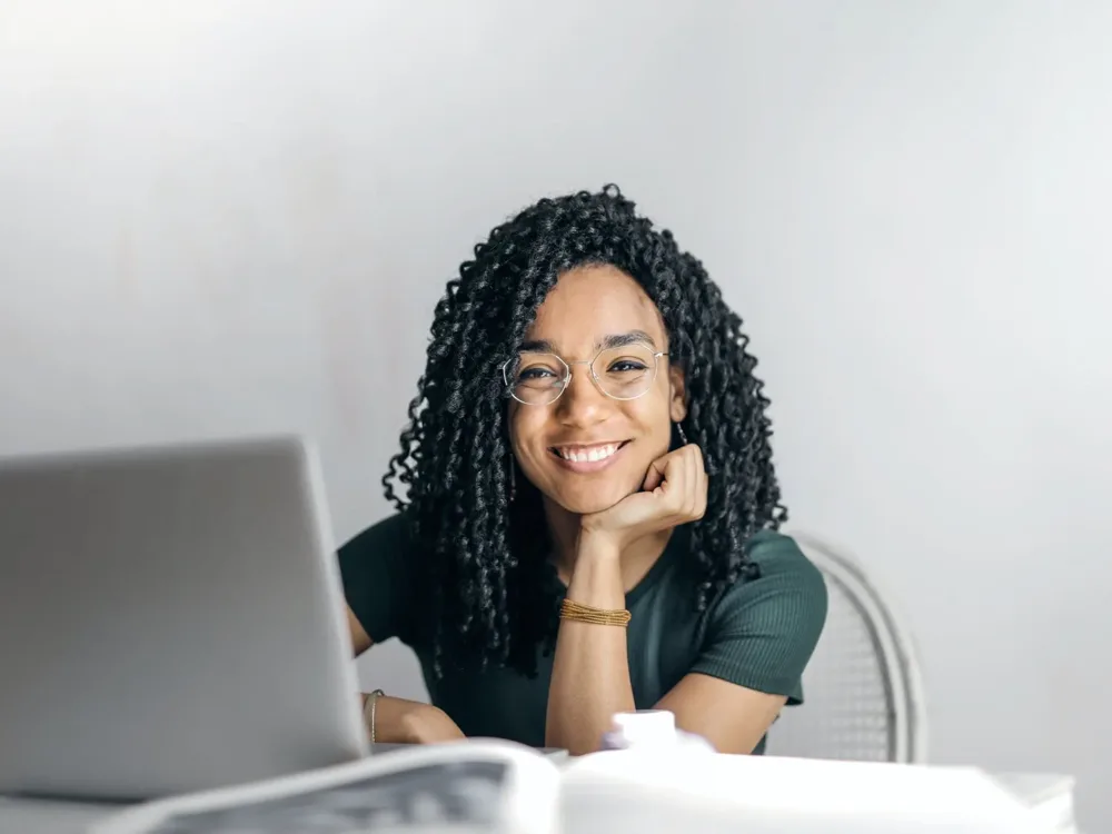 Smiling woman with curly hair and glasses at her laptop