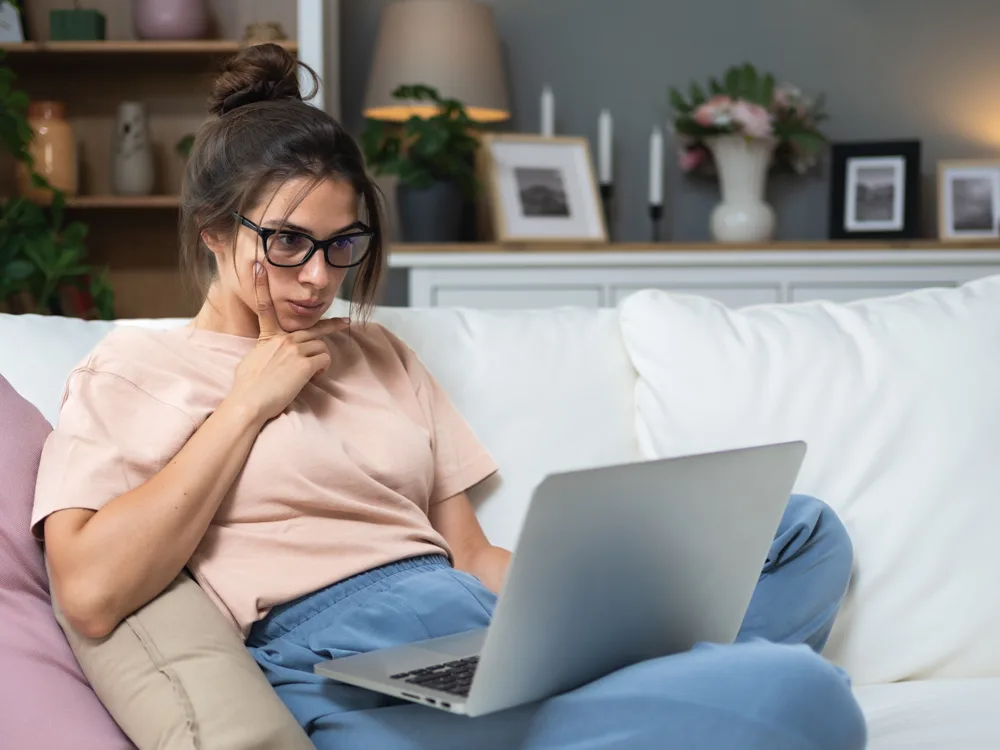 Woman in glasses on the couch looking at her laptop