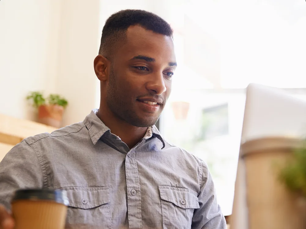 Man with a coffee cup looking at his laptop
