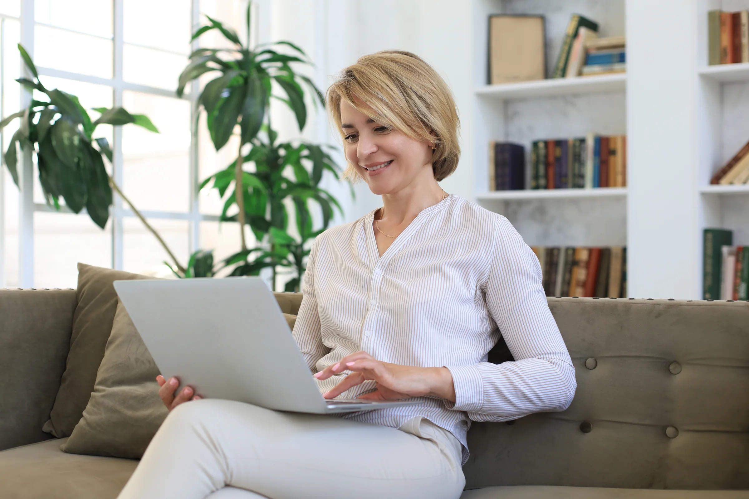 Middle-aged woman smiling at her laptop on the sofa