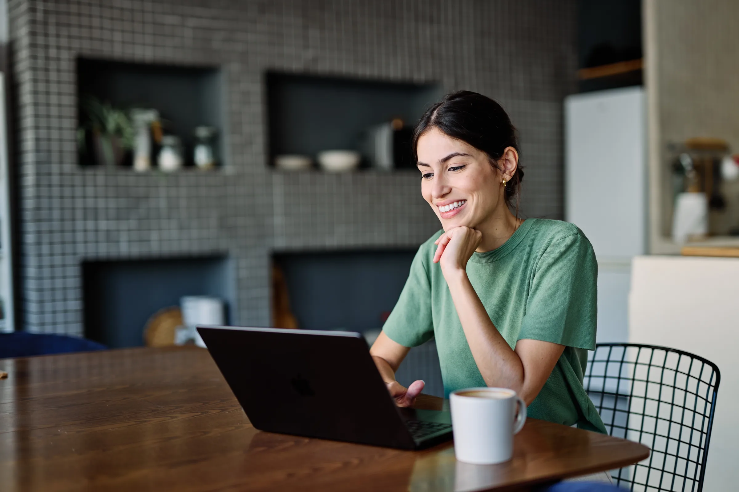 Woman smiling at her laptop at a kitchen table during a video visit