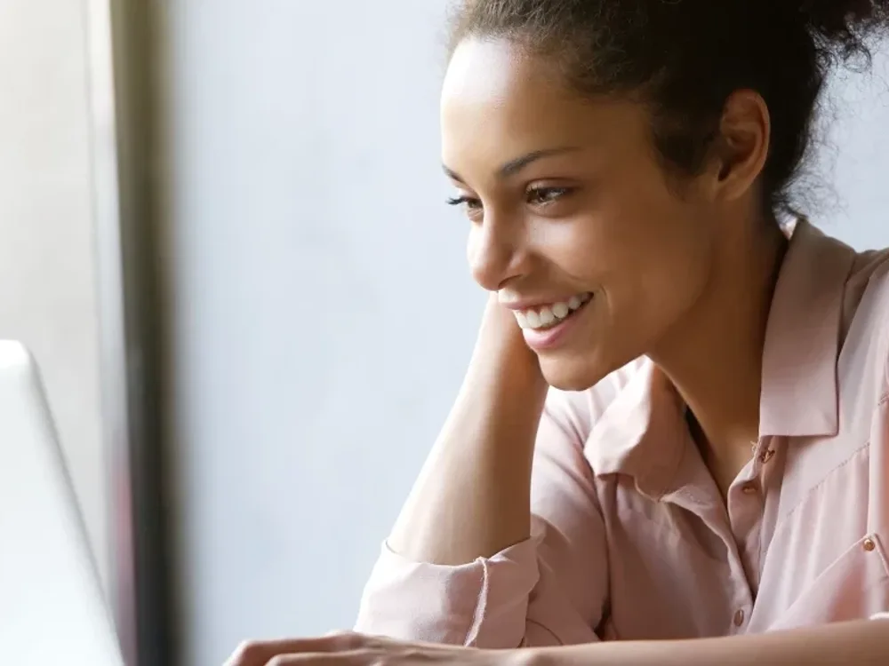 Woman smiling at her laptop by a bright window