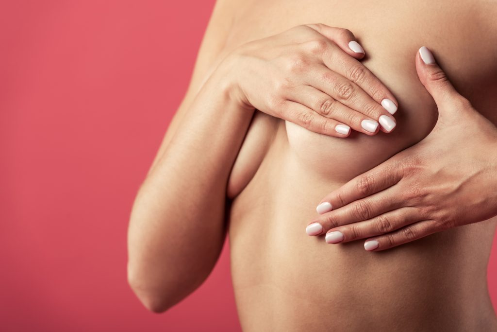 Woman cupping her breasts with both hands against a pink background