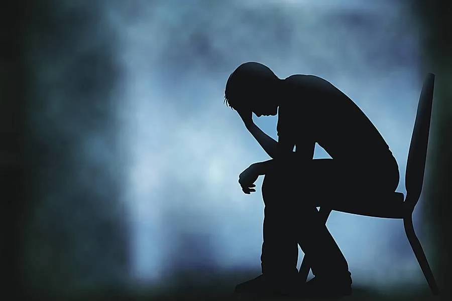 Silhouette of a person sitting with head in hands in a distressed posture