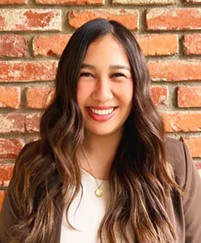Woman smiling in front of a brick wall, wearing a brown cardigan and white top
