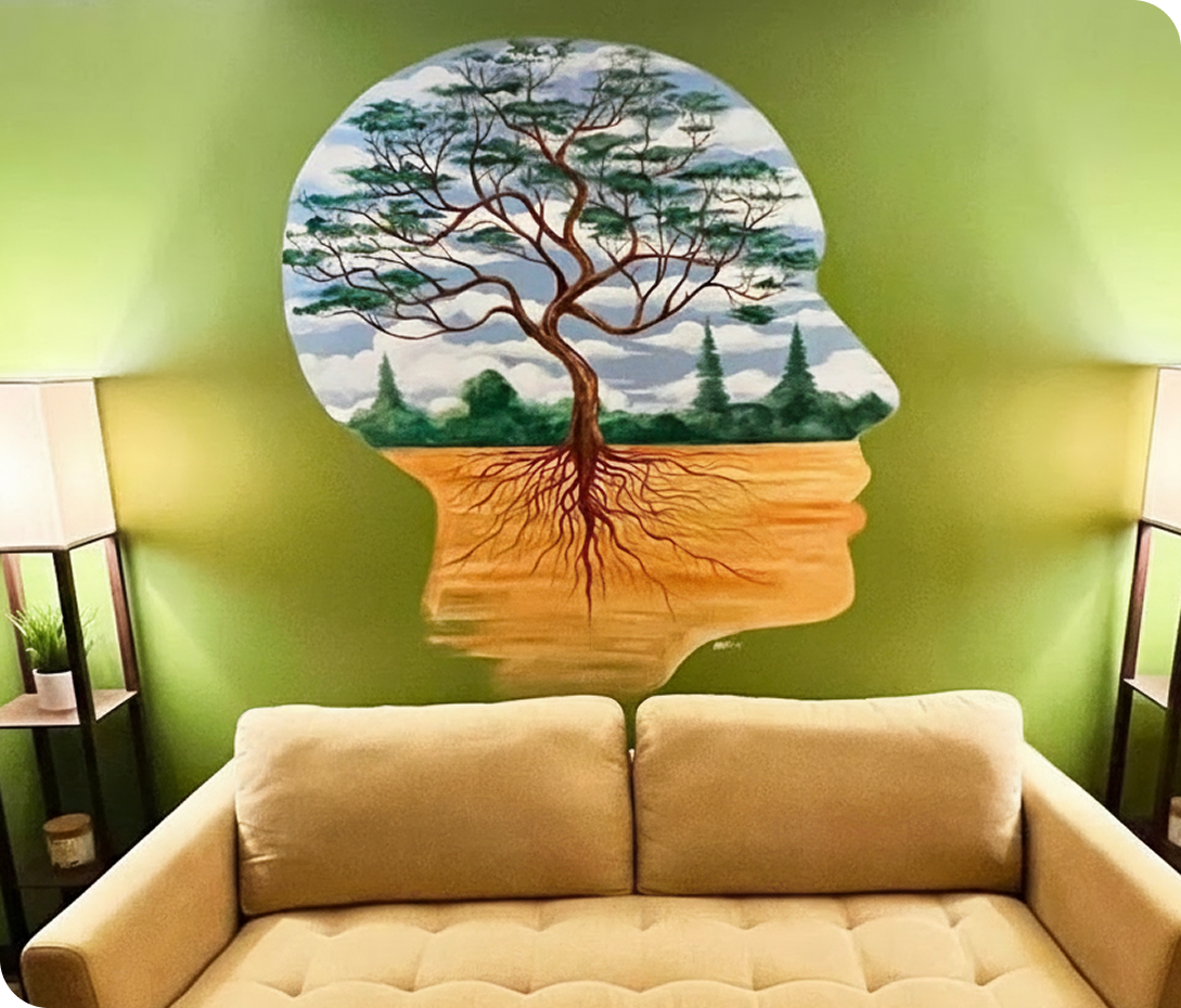 Therapy room mural of tree silhouette inside human head profile on green wall above cream sofa with side table lamps