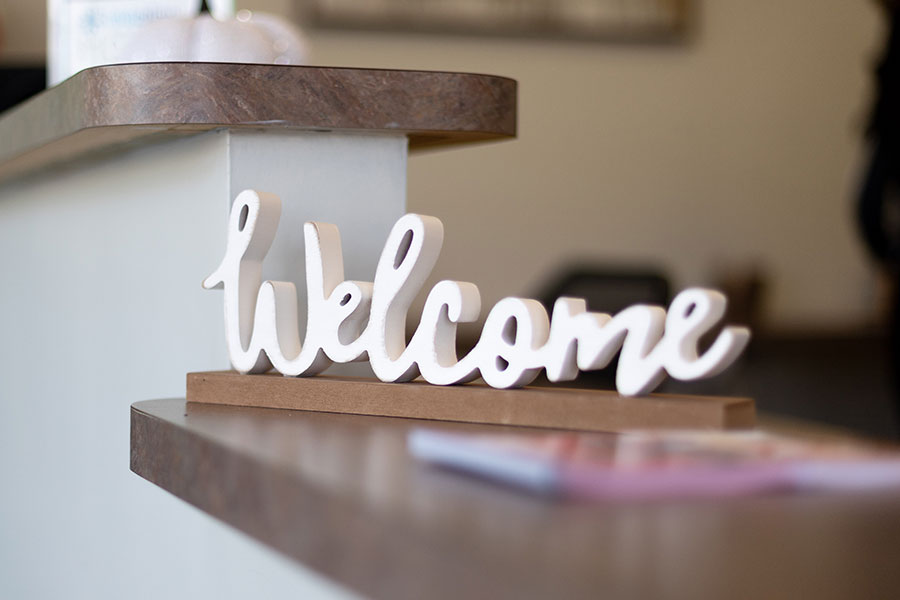 White wooden 'welcome' sign displayed on wooden shelves in a dental office reception area