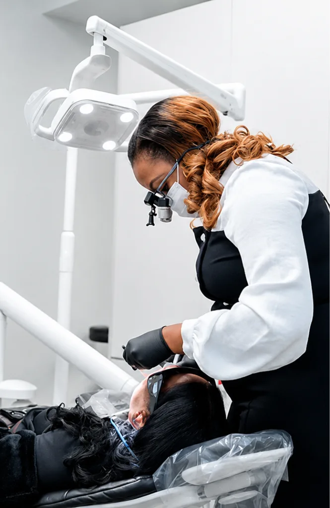 Dentist wearing magnification loupes and mask performs temporary treatment on patient under overhead surgical light