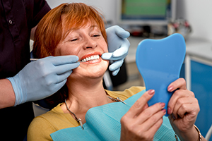Dentist examining patient's teeth with mirror during dental appointment while holding blue shade guide