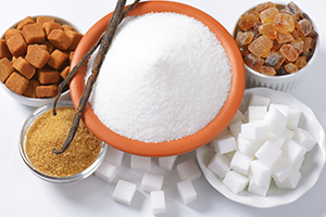 Bowl of granulated sugar surrounded by brown sugar, white sugar cubes, and other sweetener types